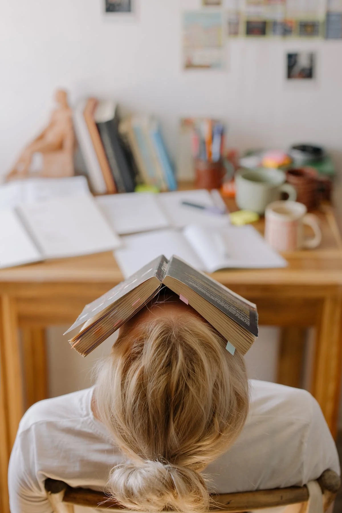 Eine Studentin am schreibtisch beim lernen zuhause mit einem buch auf kopf für eine kurze pause.